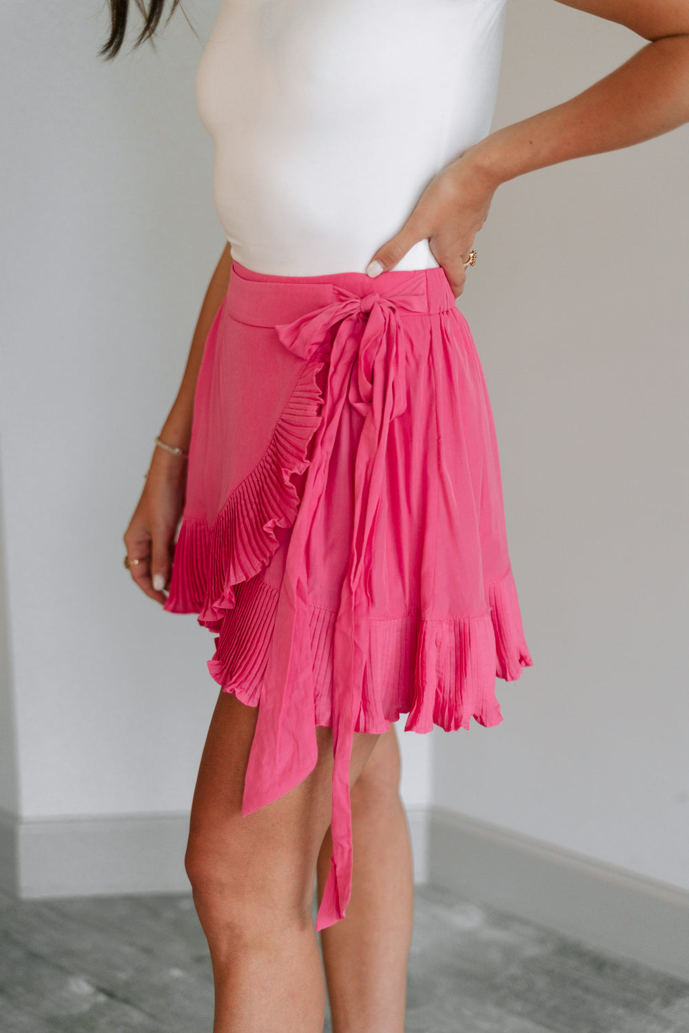 Side view of female model wearing the Gabriella Pink Ruffle Mini Skort which features Pink Lightweight Fabric, Pink Shorts Lining, Ruffle Pleated Hem Details and Side Tie Detail