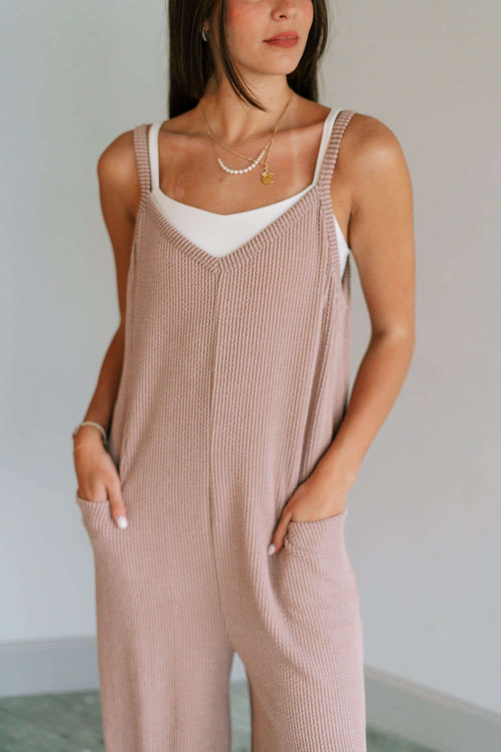 Close up view of female model wearing the Noelle Taupe Ribbed Sleeveless Jumpsuit which features Taupe Ribbed Fabric, Jogger Pant Legs, Two Side Pockets and V-Neckline