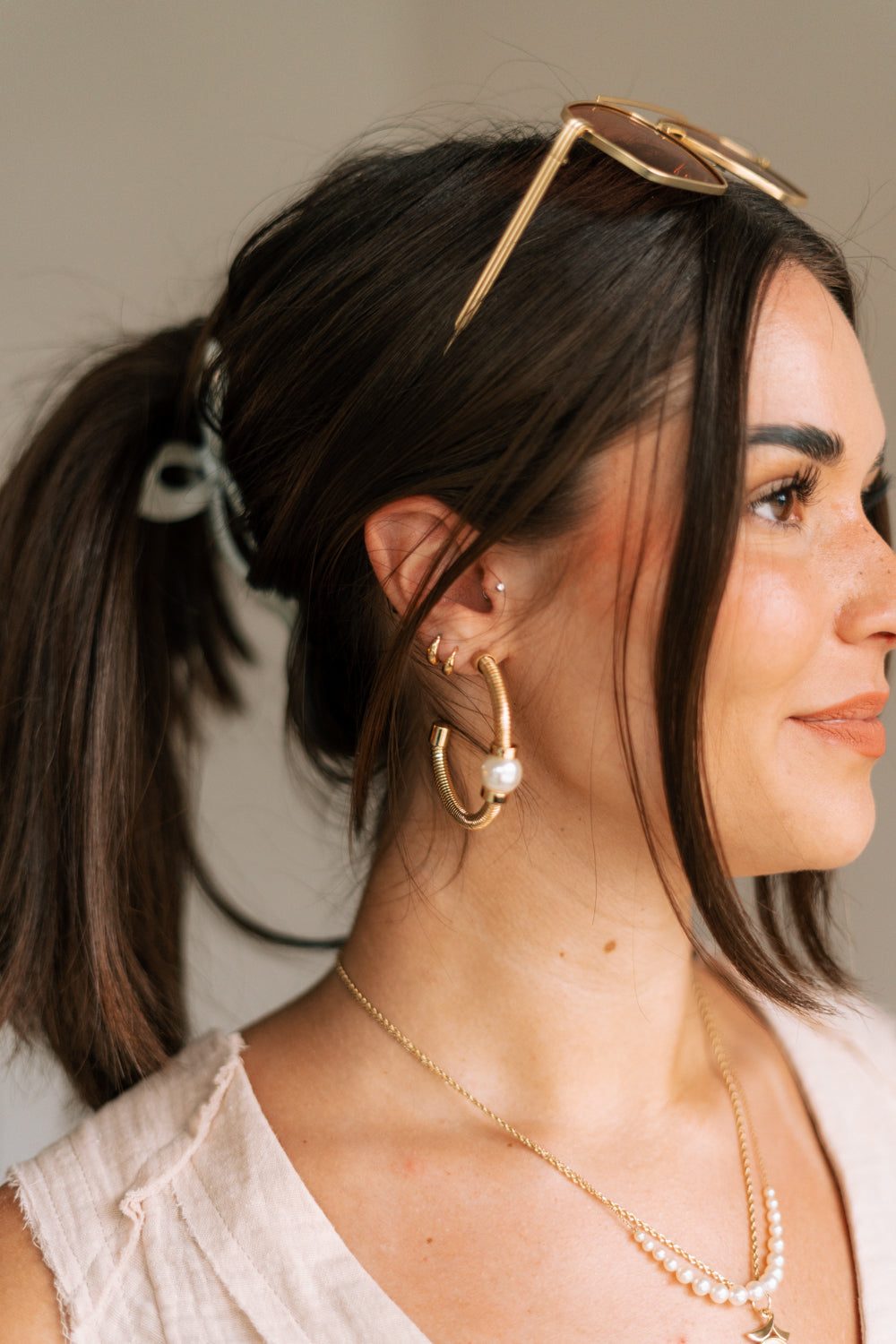 Side view of female wearing the Cora Gold Ribbed Pearl Hoop Earring which features gold ribbed open hoops with a single pearl detail