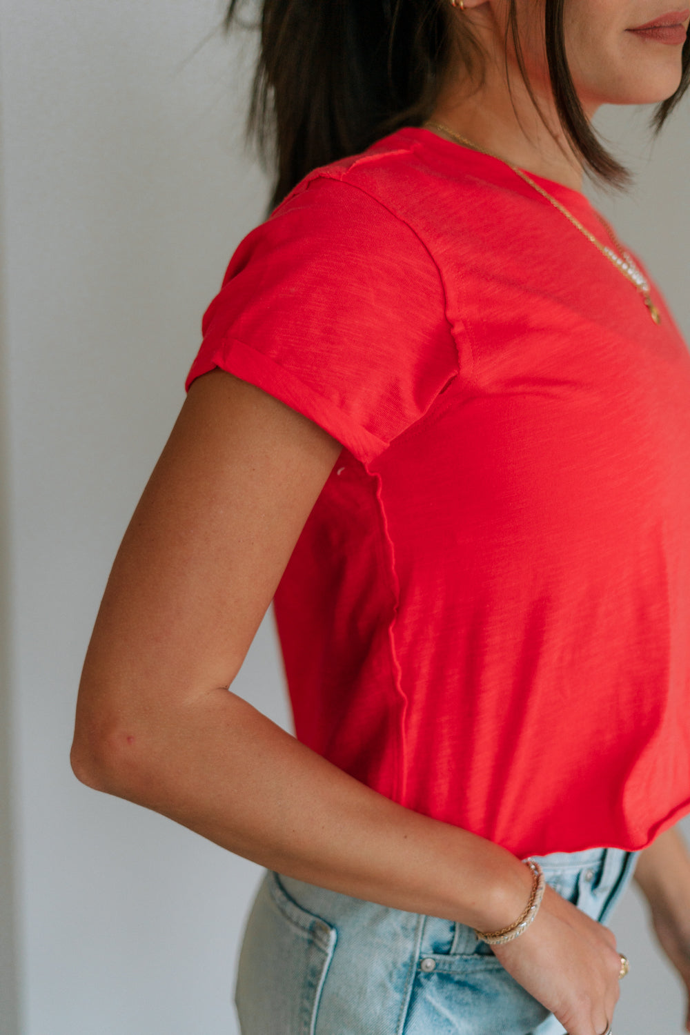 Close up side view of female model wearing the Evie Red Coral Short Sleeve Top which features Coral Red Cotton Fabric, Cropped Waist with Raw Hem, Round Neckline and Short Sleeves