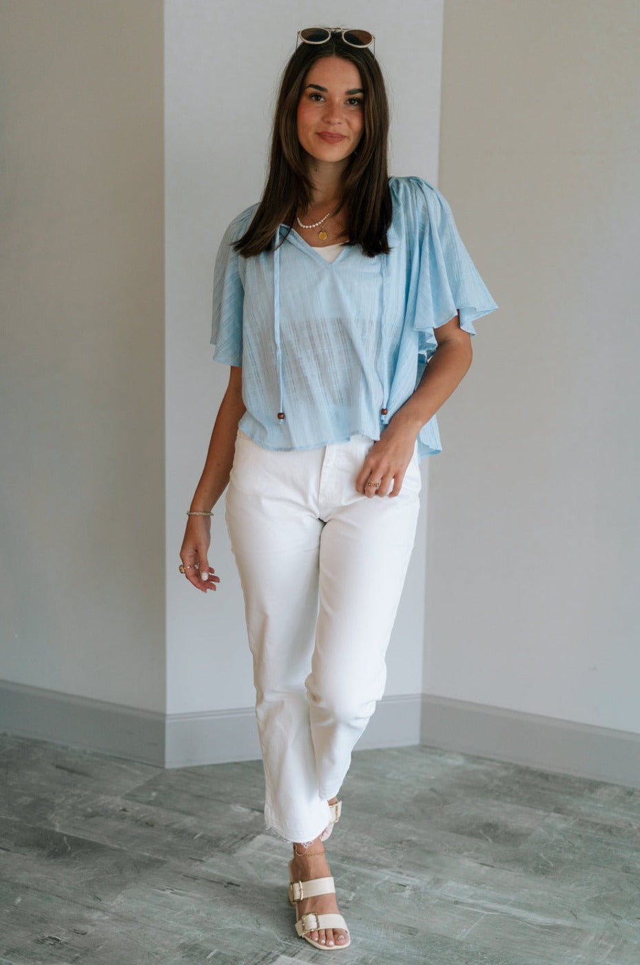Full body view of female model wearing the Danna Light Blue Short Sleeve Top which features Light Blue Cotton Fabric, Round Neckline with Tie Closure, Wooden Beads Detail and Short Sleeves