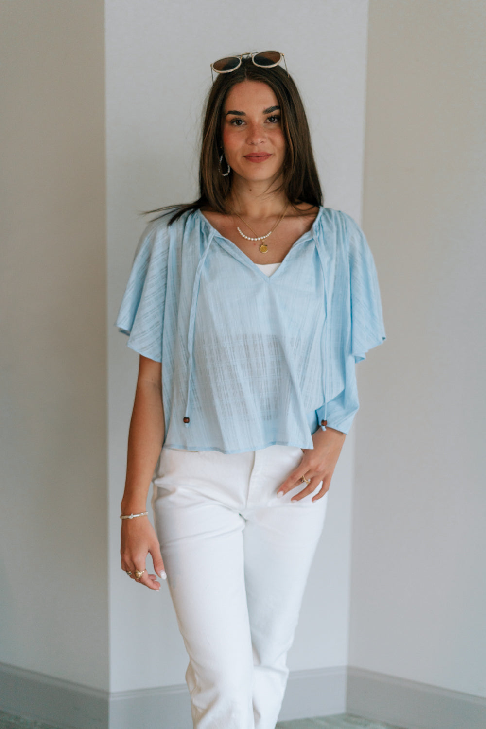 Front view of female model wearing the Danna Light Blue Short Sleeve Top which features Light Blue Cotton Fabric, Round Neckline with Tie Closure, Wooden Beads Detail and Short Sleeves