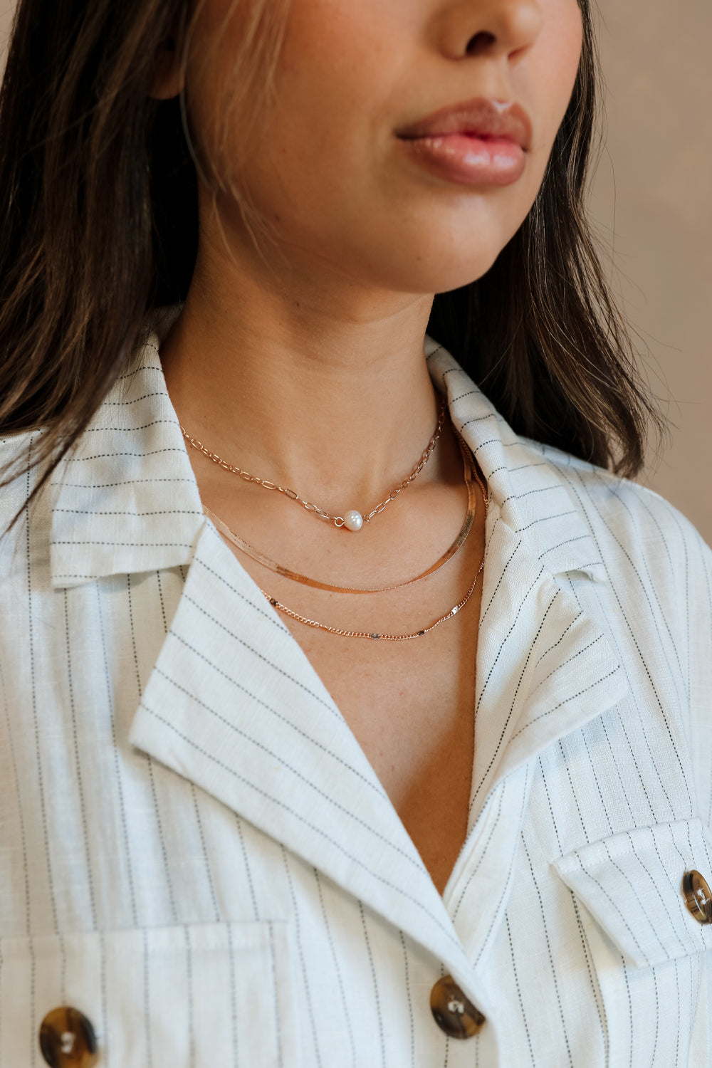 Close-up front view of model's neck; model is wearing the Madelyn Gold & Pearl Layered Necklace that has 3 varied gold chains with one pearl bead.