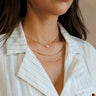 Close-up front view of model's neck; model is wearing the Madelyn Gold & Pearl Layered Necklace that has 3 varied gold chains with one pearl bead.