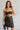 Upper body front view of model wearing the Sarah Black Strapless Mini Dress that has black fabric with metallic black florals and a strapless neckline. Model is holding black purse.