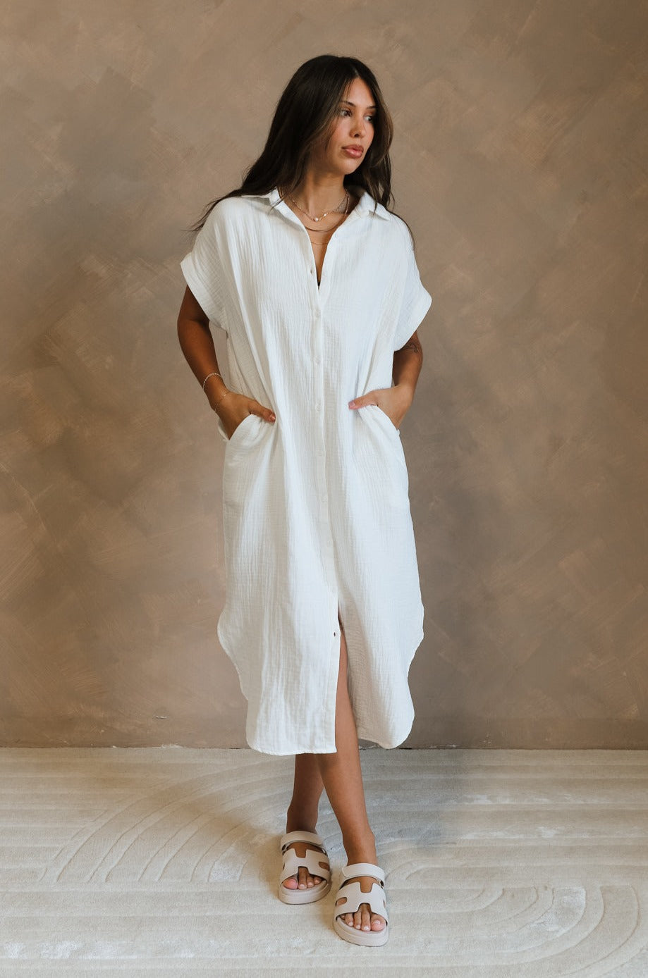 Full body front view of female model wearing the Maris White Button-Up Midi Dress that has white gauze fabric, button up front, short sleeves, and a collar. Worn white white sandals.