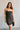 Upper body front view of model wearing the Sarah Black Strapless Mini Dress that has black fabric with metallic black florals and a strapless neckline. Model is holding black purse.