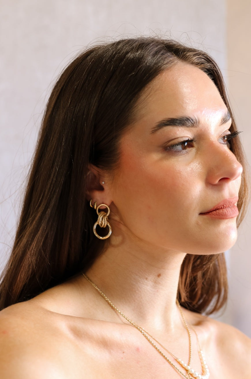 Side view of female model wearing the Lizzie Gold Circle Dangle Earrings that have matt and sparkly gold circles linked together.