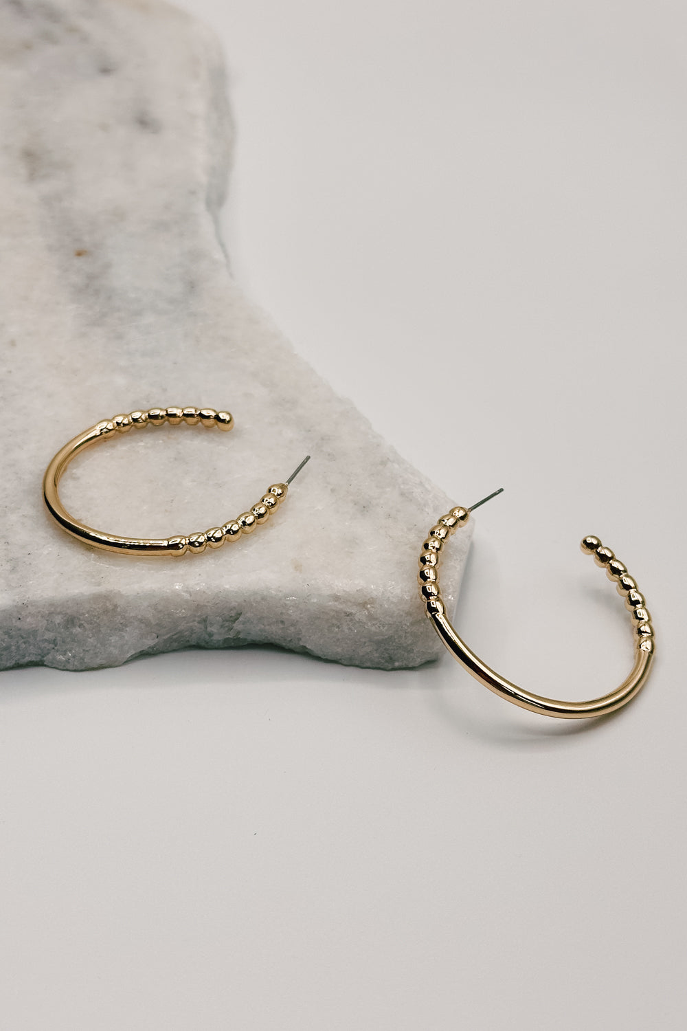 Close up view of the Alaina Gold Dipped Bead Hoop Earring. the earring features gold dipped half beaded hoops