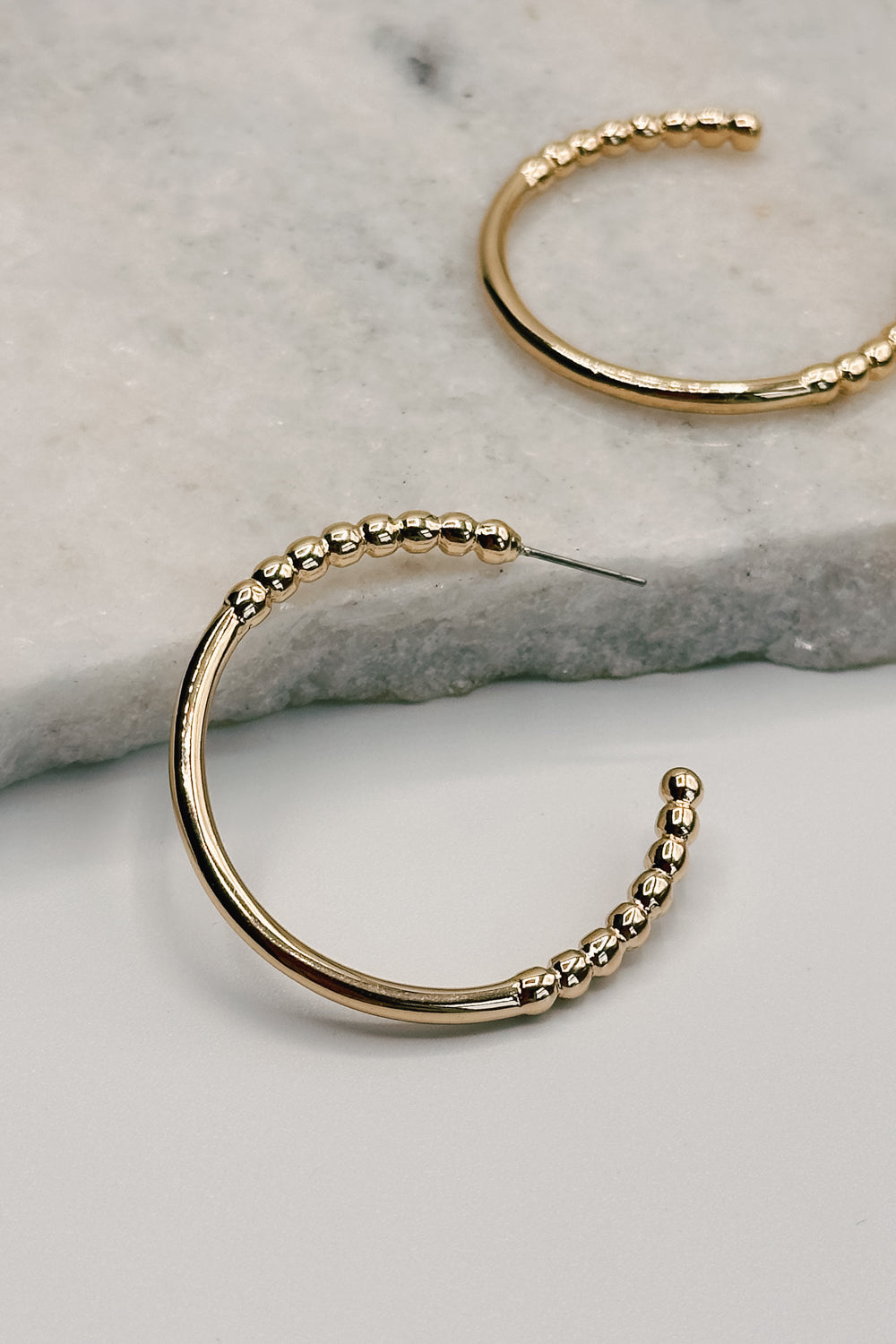Close up view of the  Alaina Gold Dipped Bead Hoop Earring. the earring features gold dipped half beaded hoops