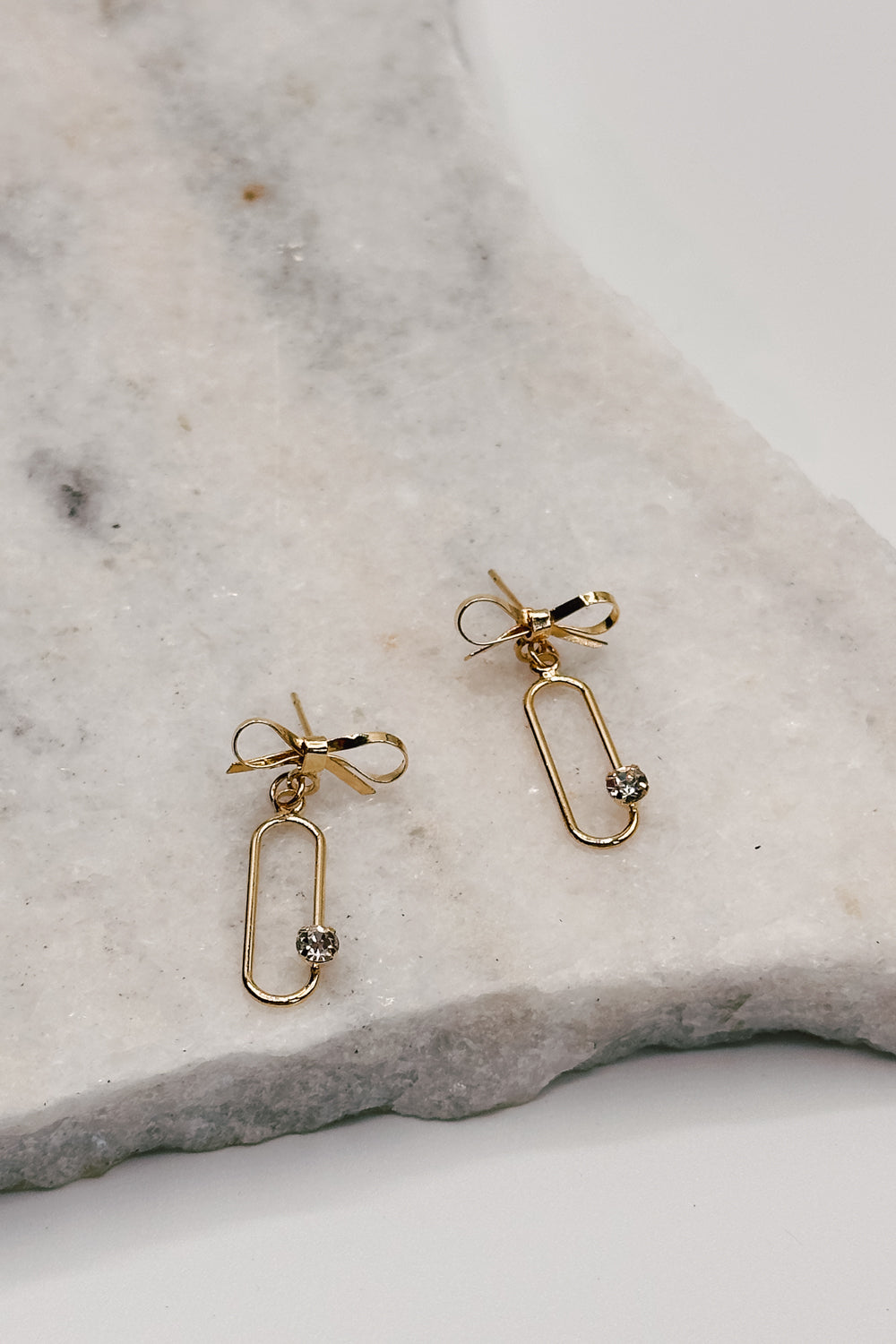 Close up view of the Ruth Gold Dipped Bow & Rhinestone Dangle Earring which features gold dipped bow studs linked with an open oval and rhinestone detail