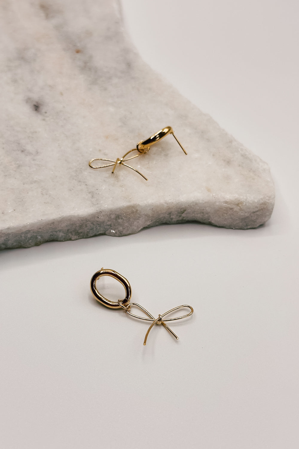 close up view of the Valeria Gold Dipped Bow Dangle Earring which features gold dipped bow shaped dangle earrings