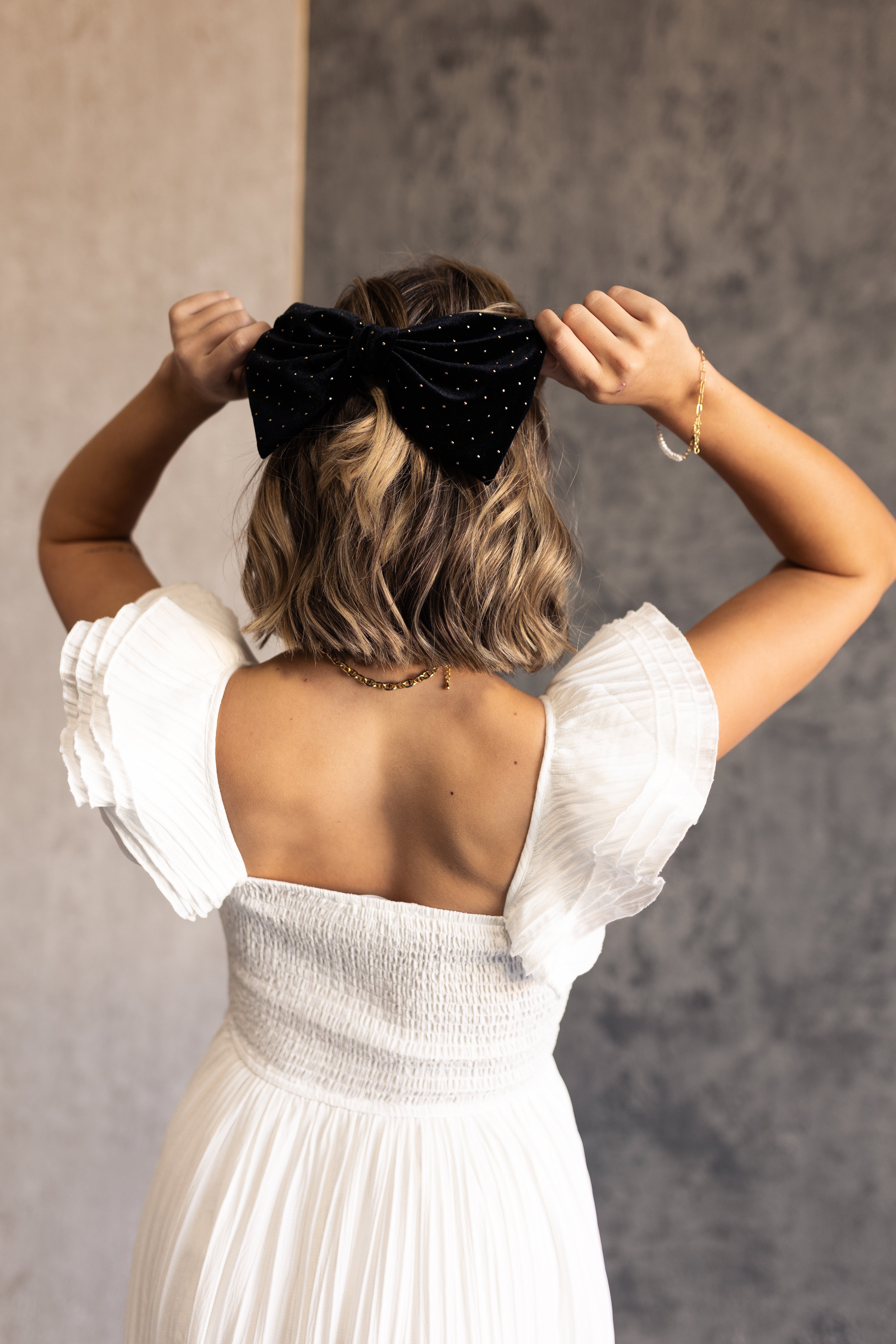 Image shows back of model's hair. Model is wearing the Stacia Black & Gold Velvet Hair Bow that features black velvet fabric with gold dot embellishments and a clasp closure.
