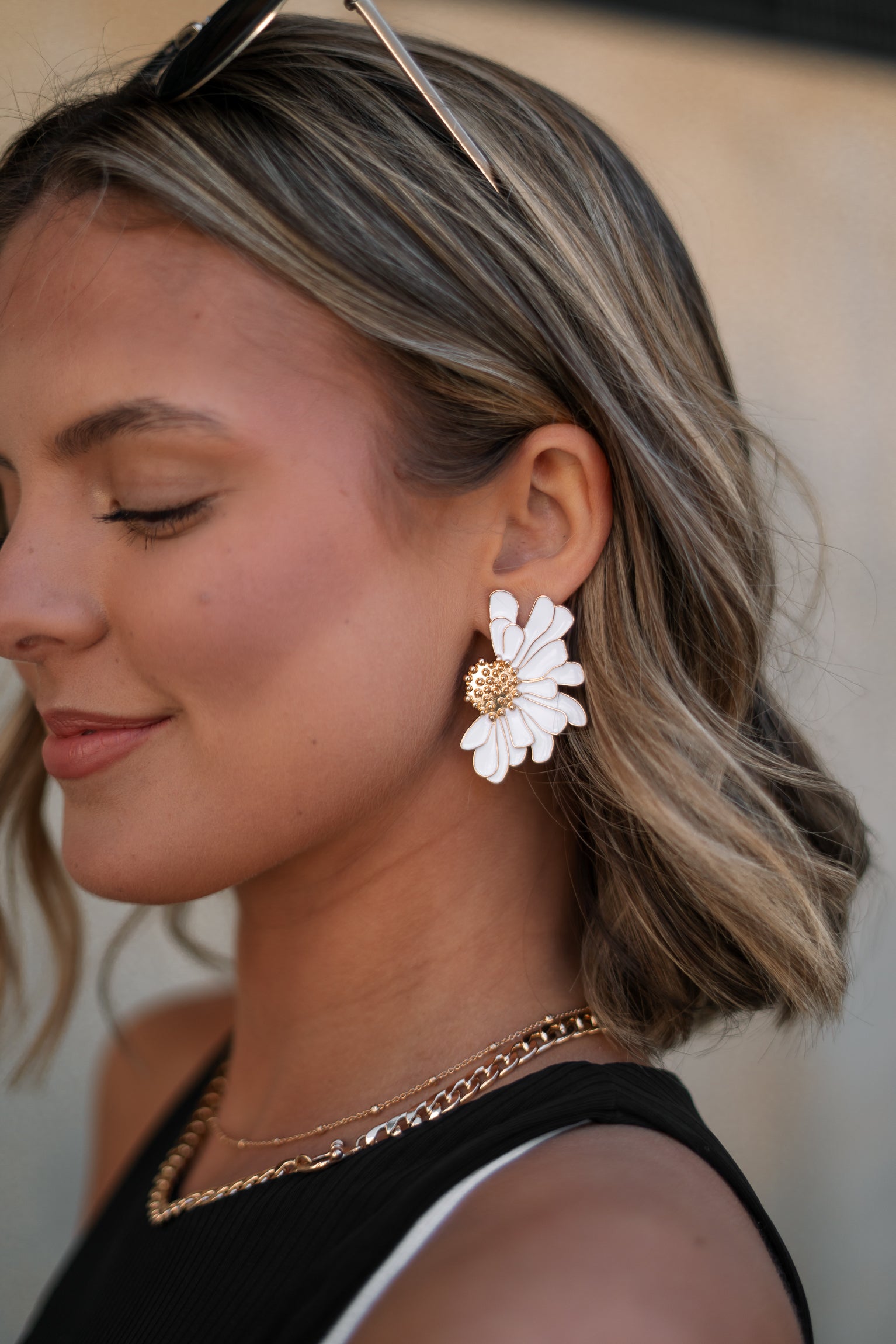 Side view of female model wearing the Chloe White & Gold Flower Stud Earring which features oversized white flower studs with gold details