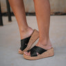 Right side view of female model wearing the Sunny Wedge Sandal in Black which features Black Faux Leather Upper, Slip-On Style and Criss-Cross Strap & Toe Wrap Detail