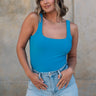 Front view of female model wearing the Sloane Blue Sleeveless Bodysuit which features Blue Lightweight Fabric, Scooped Back, Square Neckline andThong Bottom with Button Snap Closure
