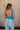 Back view of female model wearing the Sloane Blue Sleeveless Bodysuit which features Blue Lightweight Fabric, Scooped Back, Square Neckline andThong Bottom with Button Snap Closure
