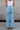 Back view of female model wearing the Kristen Light Wash Wide Leg Jeans that features wide cropped legs, light wash denim, belt loops, pockets, and a zipper/button fly. Worn with white tank top
