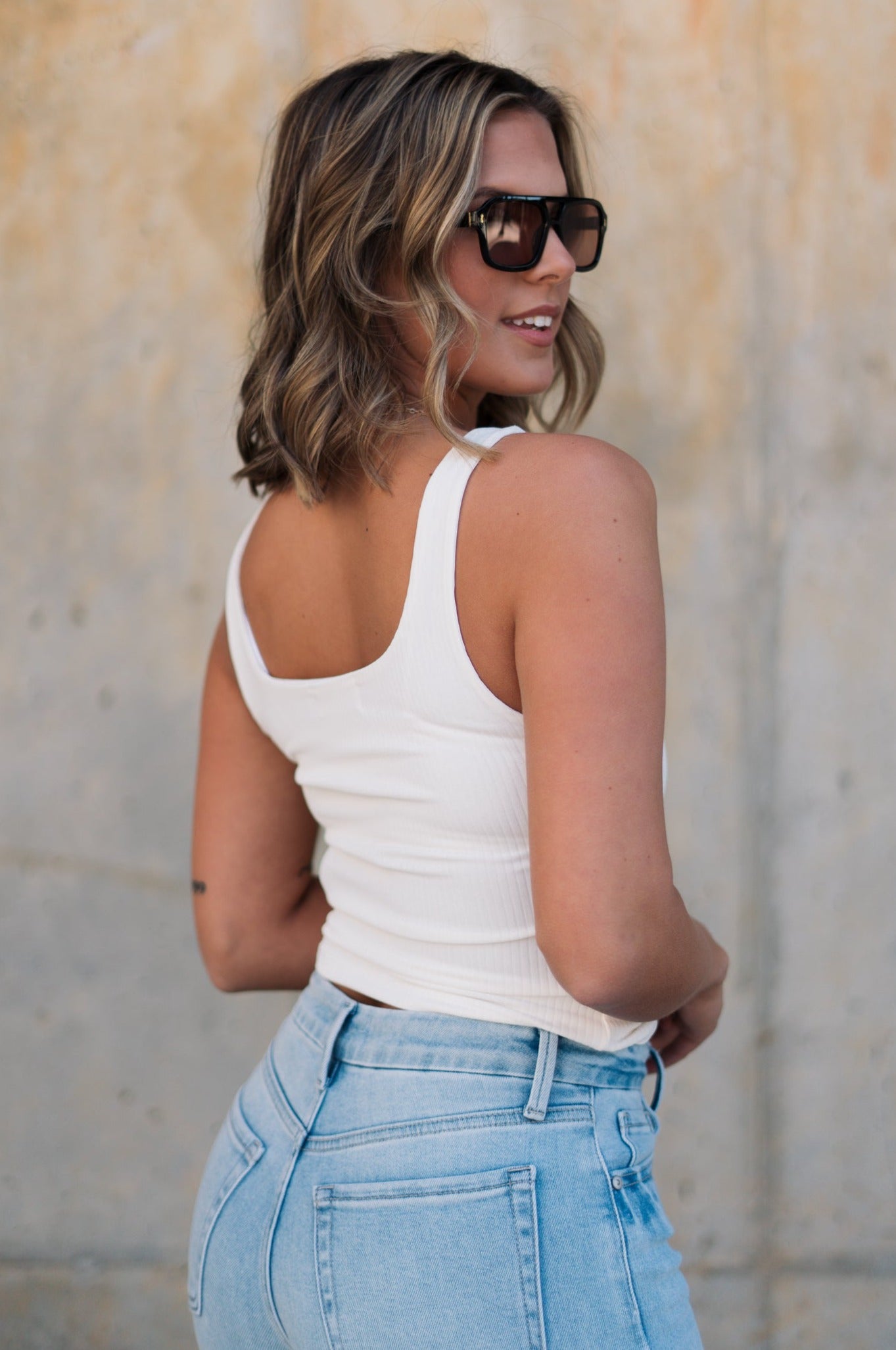 back view of female model wearing the Leigh Square Neckline Sleeveless Tank which features Ribbed Lightweight Fabric, Square Neckline and Sleeveless. the tank is available in white and black.