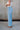 Side view of female model wearing the Kristen Light Wash Wide Leg Jeans that features wide cropped legs, light wash denim, belt loops, pockets, and a zipper/button fly. Worn with white tank top
