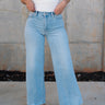 Front view of female model wearing the Kristen Light Wash Wide Leg Jeans that features wide cropped legs, light wash denim, belt loops, pockets, and a zipper/button fly. Worn with white tank top