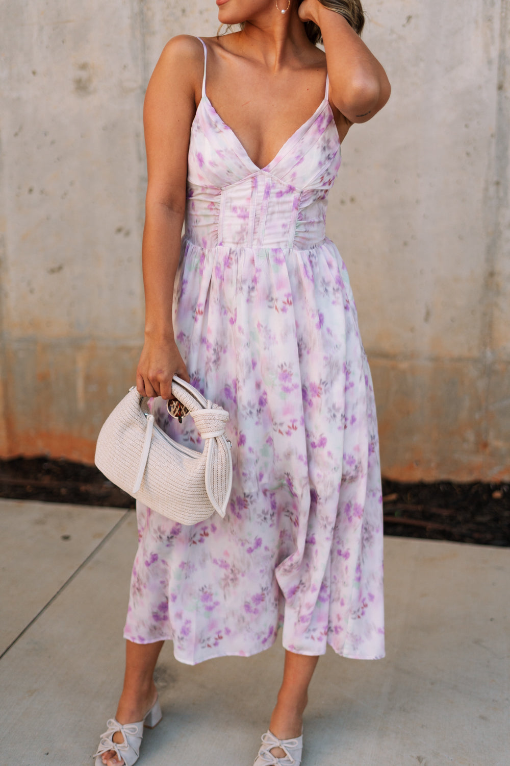 front view of female model wearing the Bridget Lavender Watercolor Midi Dress that has a lavender watercolor floral pattern, a corset top, thin straps, and midi length
