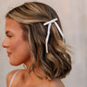 Side view of female model's hair; model is wearing the Melrose Hair Bow Barette in cream that has a barrette with a thin ivory bow..