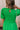 Upper body back view of female model wearing the Lea Green Puff Sleeve Mini Dress that has kelly green fabric, a smocked upper with high neck, short puff sleeves, and mini length. Model is holding coffee and has purse on shoulder.