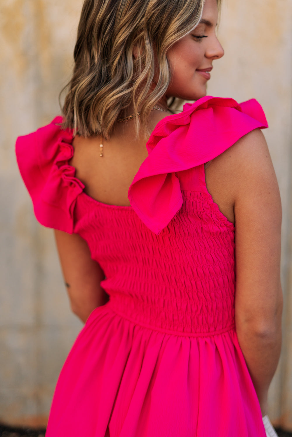 Upper body back view of female model wearing the Kristina Pink Smocked Sleeveless Midi Dress that has hot pink fabric, side slit pockets, midi length, smocked upper, a scoop neckline, and ruffled straps.