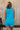 Back view of female model wearing the Chelsea Blue Sleeveless Romper that has bright blue fabric, a v neck, side pockets, and thick straps. 