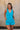 Front view of female model wearing the Chelsea Blue Sleeveless Romper that has bright blue fabric, a v neck, side pockets, and thick straps. Model has hands in pockets.