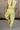 Back view of female model wearing the Alexis Green Sleeveless Jogger Jumpsuit which features Light Green Knit Fabric, Jogger Pant Legs, Side Pockets, Drawstring Tie Waistband and overlap Open Back with Button Closure