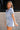 Side view of female model wearing the Mavis Denim Short Sleeve Zip-Up Romper which features Denim Fabric, Two Front Pockets, Front Zipper Closure, Adjustable Monochrome Belt with Loops, Collared Neckline and Short Sleeves