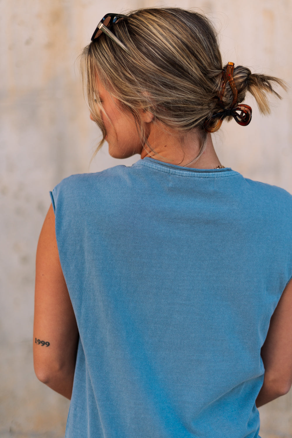 Close-up upper body back view of female model wearing the Celia Blue Knit Mini Dress that has slate blue knit fabric, a round neck, sleeveless body, and mini length.