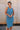 front view of female model wearing the Paula Blue Ribbed Midi Dress that has ribbed medium blue fabric, a round neck, sleeveless, and midi length hem. 