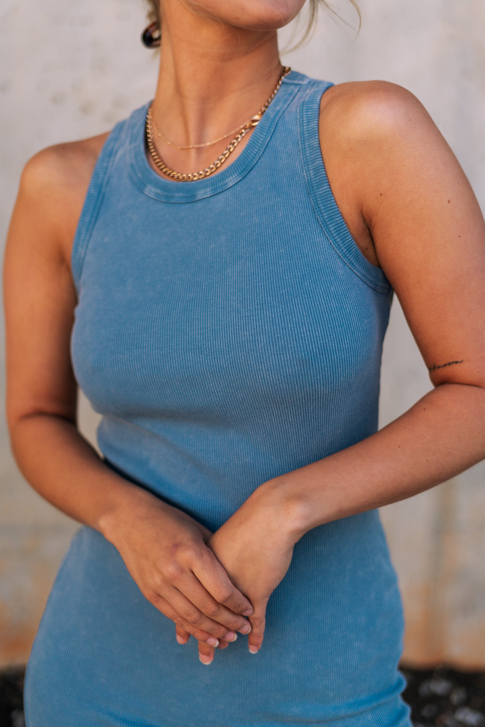 Upper body front view of female model wearing the Paula Blue Ribbed Midi Dress that has ribbed medium blue fabric, a round neck, sleeveless, and midi length hem. 