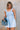 front view of female model wearing the Taylor Light Wash Denim Romper that has light wash denim fabric, straps with frayed hems, elastic waist, neckline pleating, and side pockets.