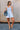 Full body front view of female model wearing the Taylor Light Wash Denim Romper that has light wash denim fabric, straps with frayed hems, elastic waist, neckline pleating, and side pockets.