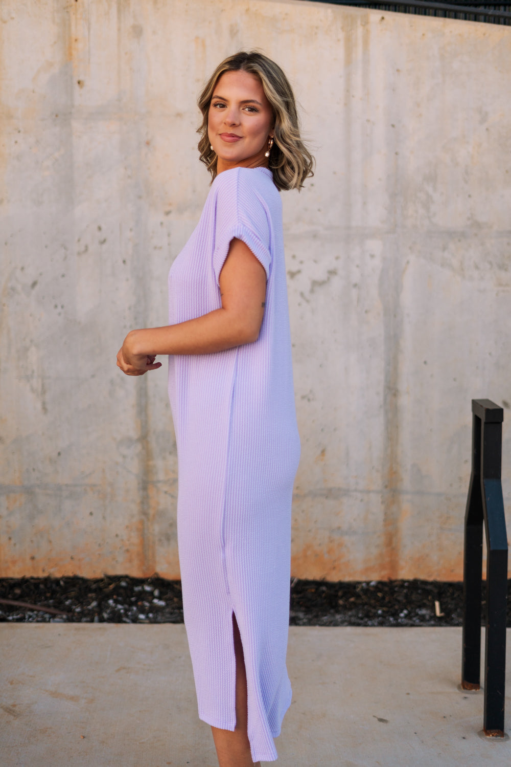 Full body side view of female model wearing the Luna Lavender Ribbed Midi Dress which features Lavender Ribbed Fabric, Midi Length, Slit Side Details, Round Neckline and Short Sleeves
