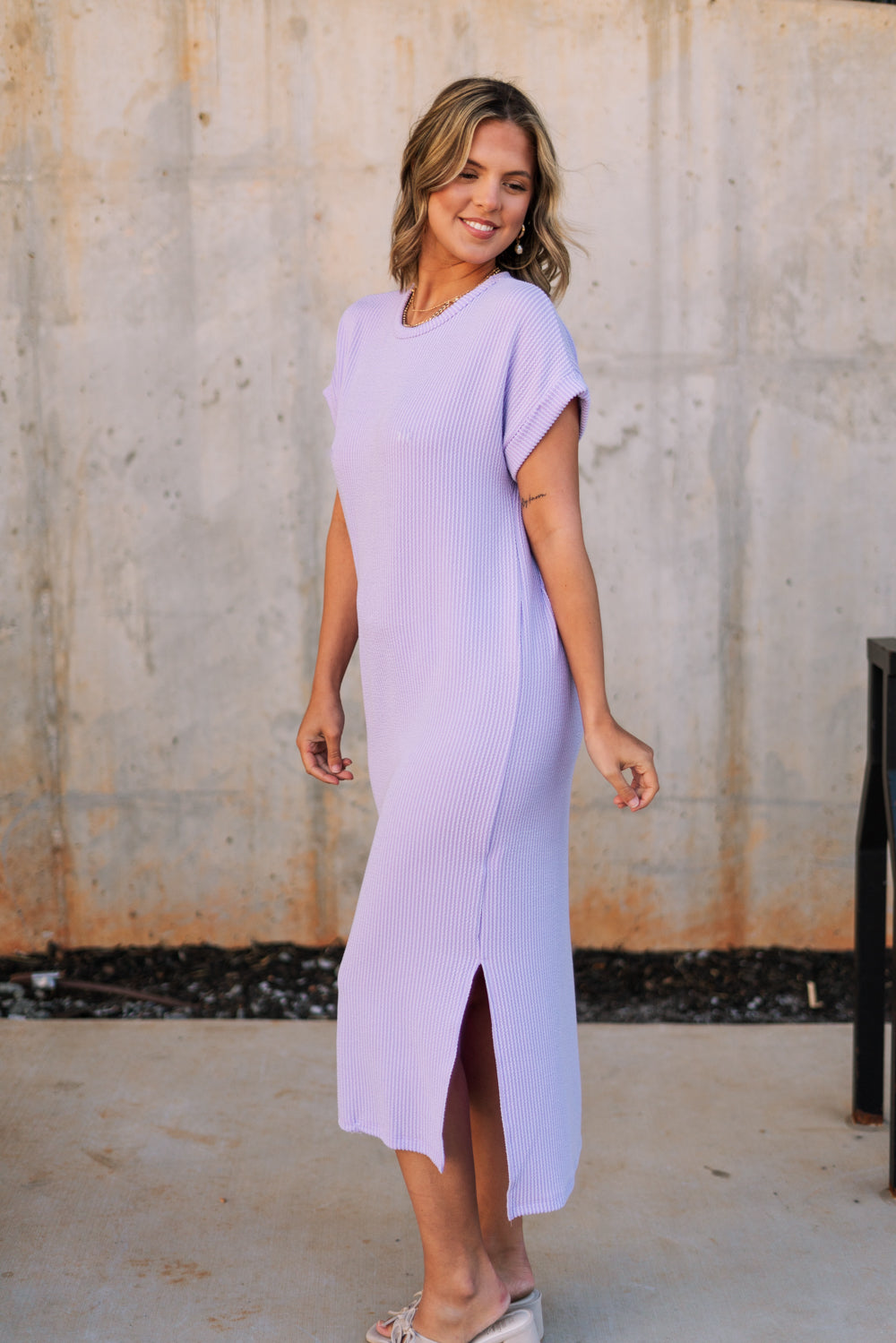 Full body side view of female model wearing the Luna Lavender Ribbed Midi Dress which features Lavender Ribbed Fabric, Midi Length, Slit Side Details, Round Neckline and Short Sleeves