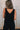 Upper body back view of female model wearing the Kinsley Black Sleeveless Jumpsuit that has black lightweight fabric, thick straps, wide legs, and a v-neck.