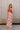 Full body side view of female model wearing the Cali Rust & Cream Cutout Floral Jumpsuit that has a rust upper with a halter neckline, midriff cutouts with a ring in center, and white wide leg pants with rust floral print.