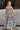 Full body front view of female model wearing the Leilani Printed Sleeveless Maxi Dress that has a multi-colored green, red, pink, purple, and yellow print, spaghetti straps, a smocked upper, and a tiered skirt.