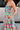 Close-up upper body side view of female model wearing the Leilani Printed Sleeveless Maxi Dress that has a multi-colored green, red, pink, purple, and yellow print, spaghetti straps, a smocked upper, and a tiered skirt.
