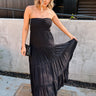 Full body front view of female model wearing the Amaya Black Strapless Maxi Dress that has a smocked upper and a tiered skirt. Model is holding skirt