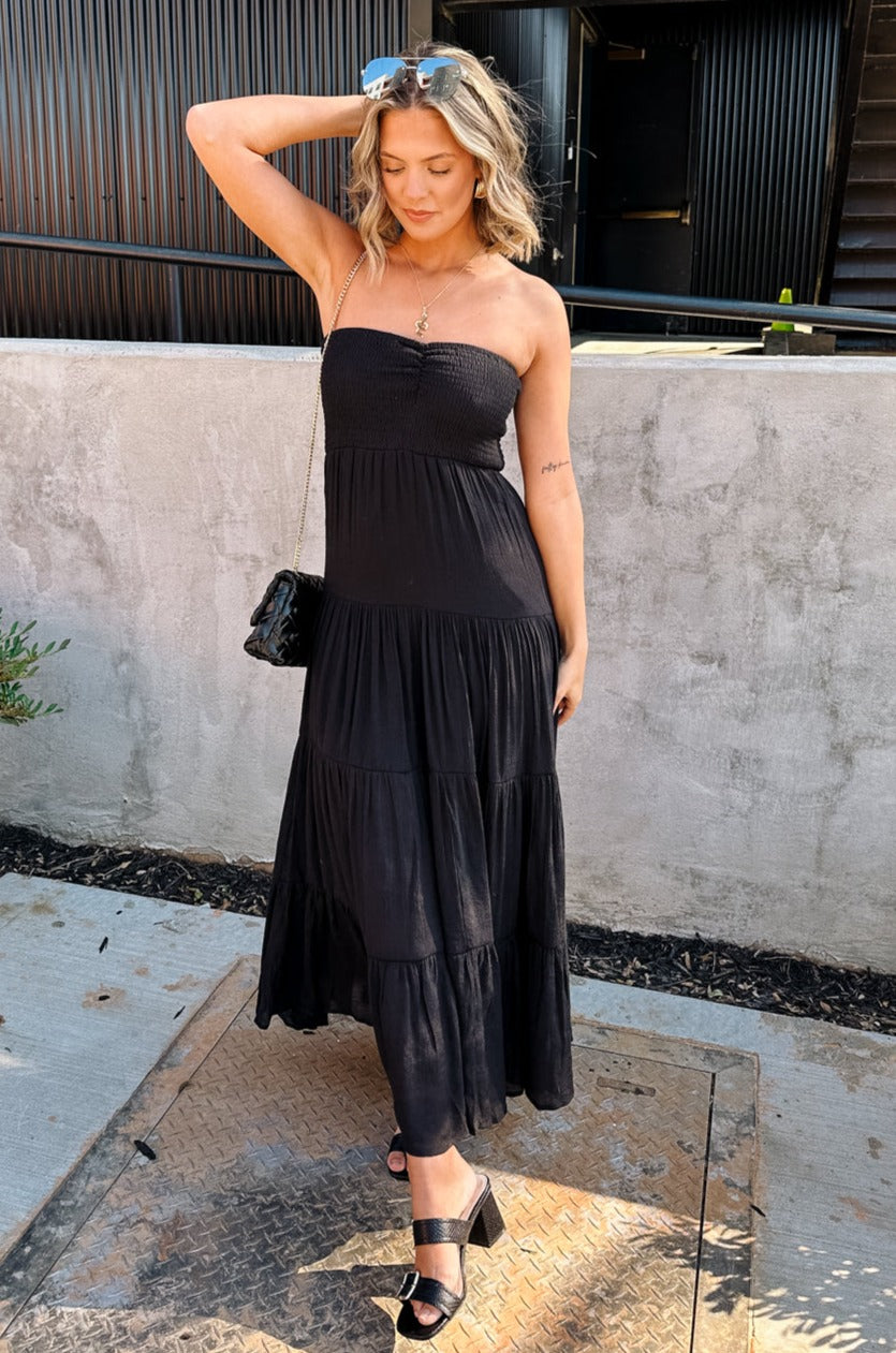 Full body front view of female model wearing the Amaya Black Strapless Maxi Dress that has a smocked upper and a tiered skirt