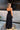 Full body back view of female model wearing the Amaya Black Strapless Maxi Dress that has a smocked upper and a tiered skirt