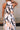 Upper body back view of female model wearing the Elina Printed Button Front Midi Dress that has ivory, black, and orange geometric printing, a tie belt, a button up front, a collared sleeveless neckline, and midi length.