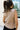 Back view of female model wearing the Cecilia Taupe Padded Shoulder Tank that has taupe knit fabric, a round neck, and padded sleeveless shoulders.