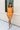Full body front view of female model wearing the Raya Orange Denim Romper that has orange denim fabric, button up front, belt, and ruffle details.